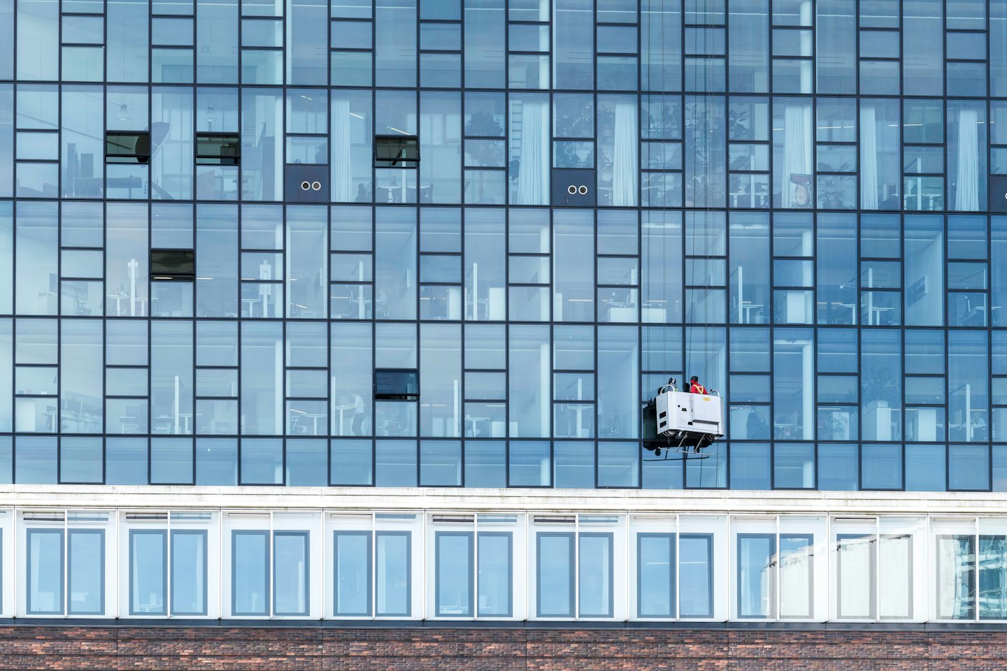 Window cleaner on a suspended gondola washes a modern building.